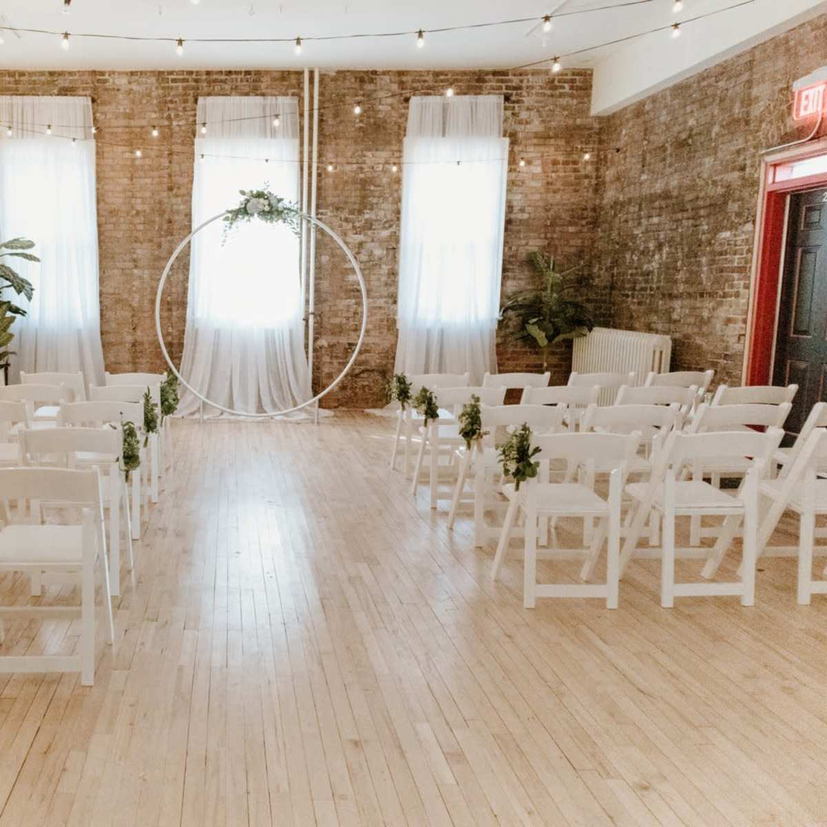 A spacious event venue with white chairs arranged in two rows facing a circular decoration near a large window.