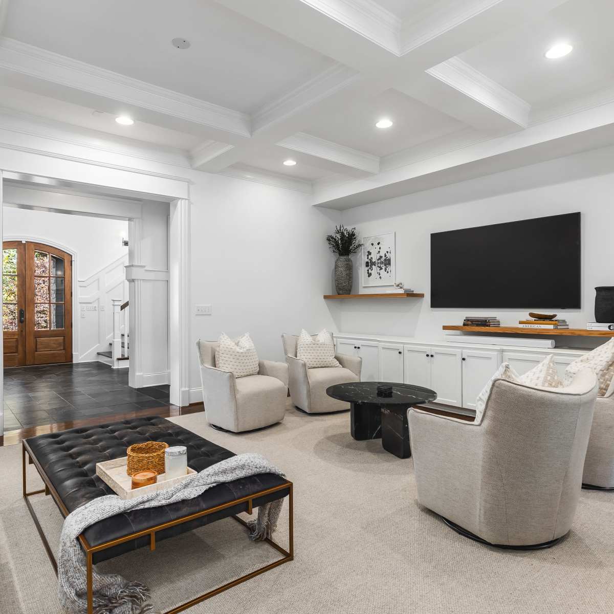 A modern living room with a light-colored furniture setup, a large television mounted on the wall, and decorative wall art framed in a gallery style.