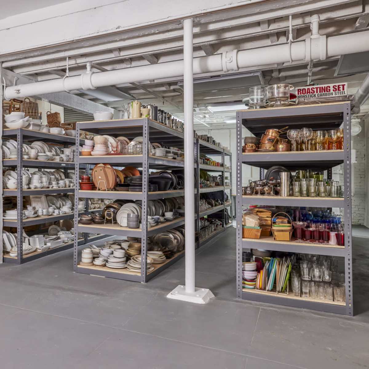 A spacious warehouse filled with metal shelving units displaying various kitchenware, including dishes, serving sets, and storage containers.