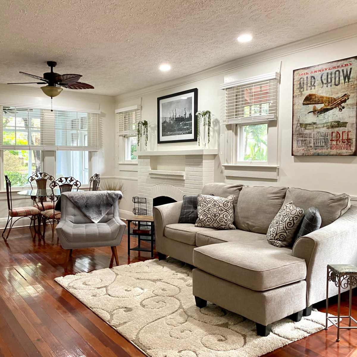 A well-lit living room with a gray sectional sofa, a decorative chair, and a coffee table on a light-colored rug, featuring a fireplace and a large wall art piece.