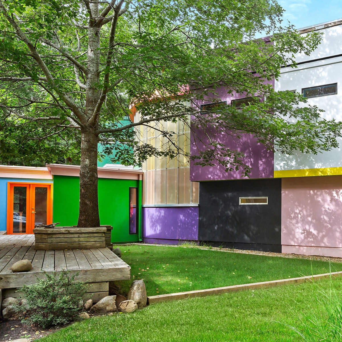 A modern house featuring geometric shapes and vibrant colors, surrounded by green grass and trees.