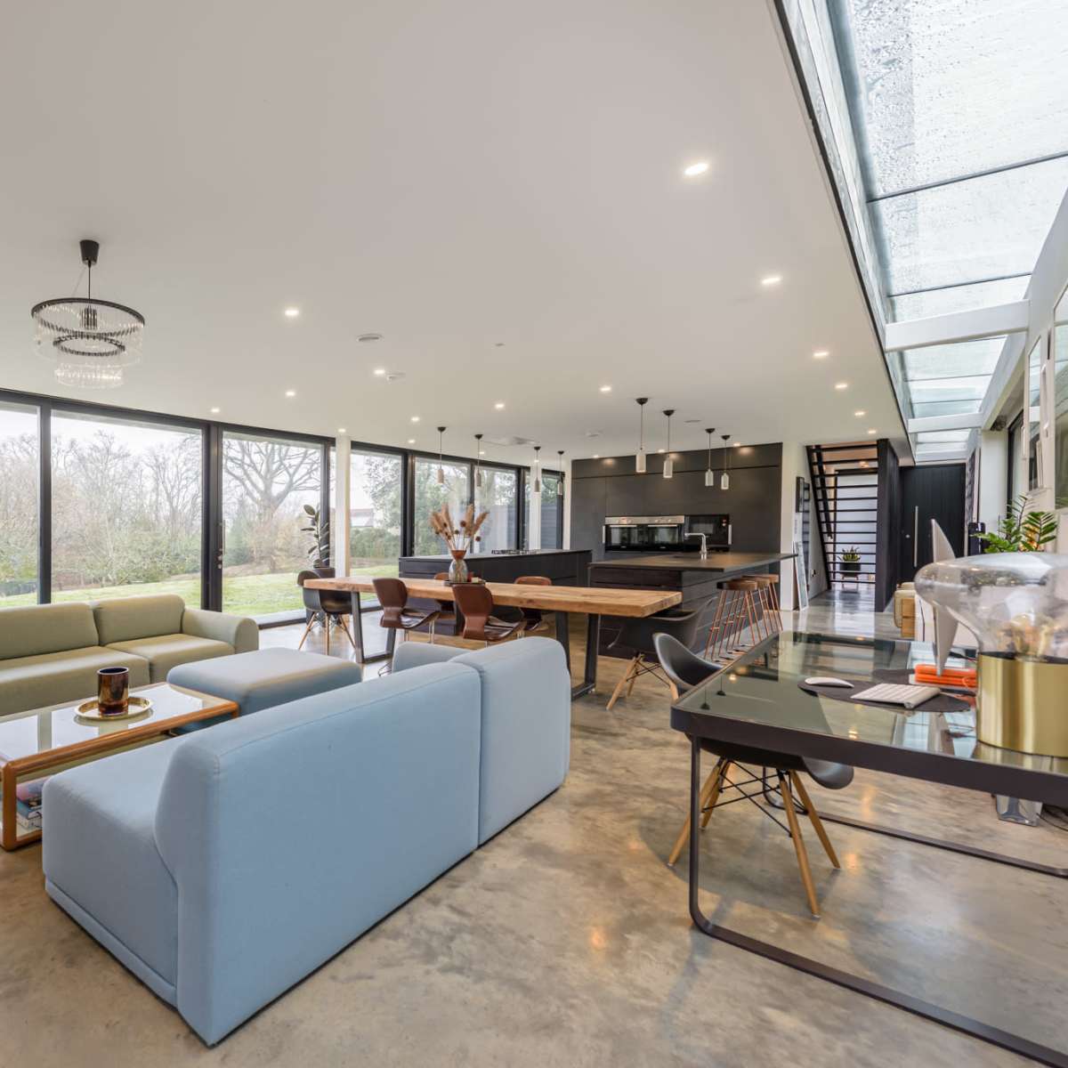 A modern open-plan living space with large windows, a dining area, and contemporary furnishings, including a blue sofa and a wooden dining table.