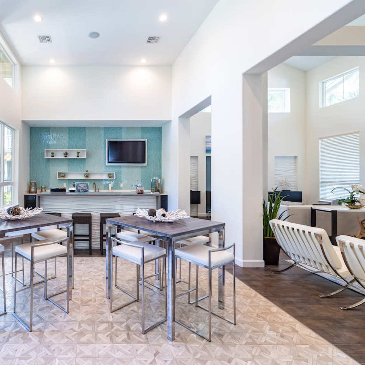 A modern, open-concept room with a kitchen area, dining tables, and large windows allowing natural light.