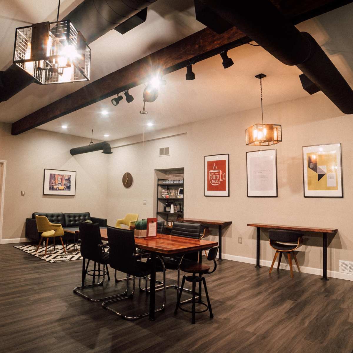 A modern, open room with wooden beams, a dining table, seating area, and framed artwork on the walls.
