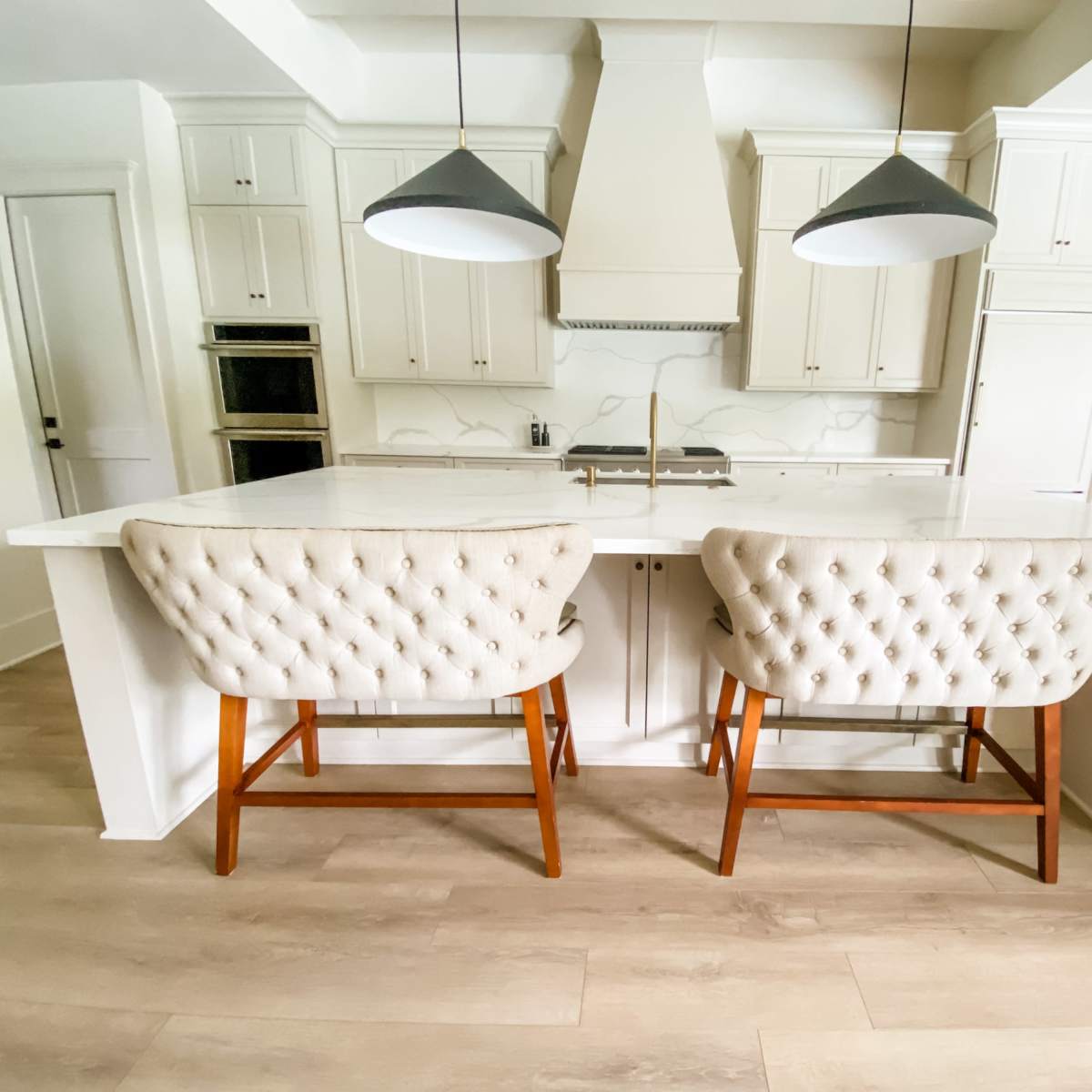 A modern kitchen with a central island featuring two tufted bar stools and pendant lighting above.