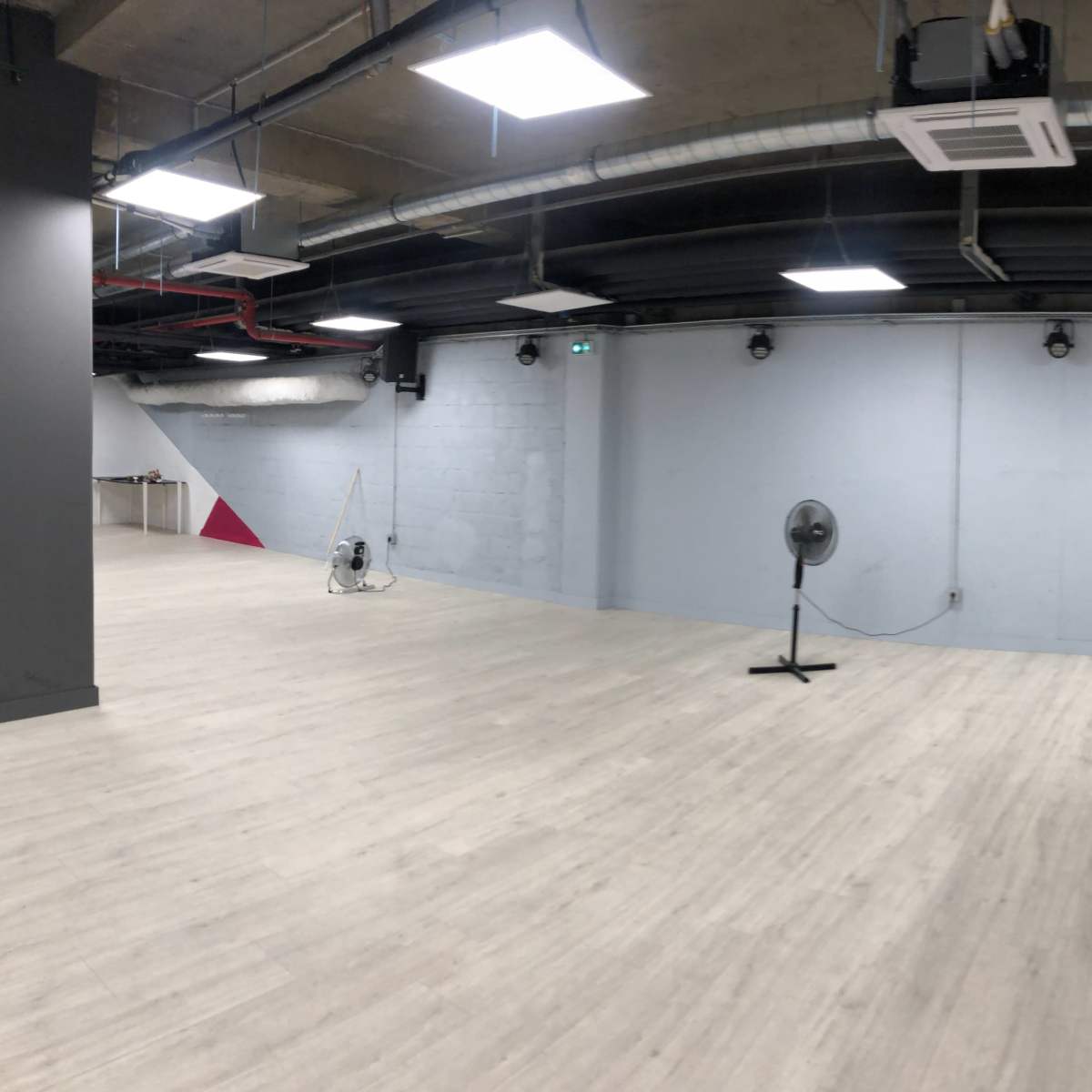 An empty industrial-style room with light wooden flooring and a wall featuring a geometric pattern of black and red sections.