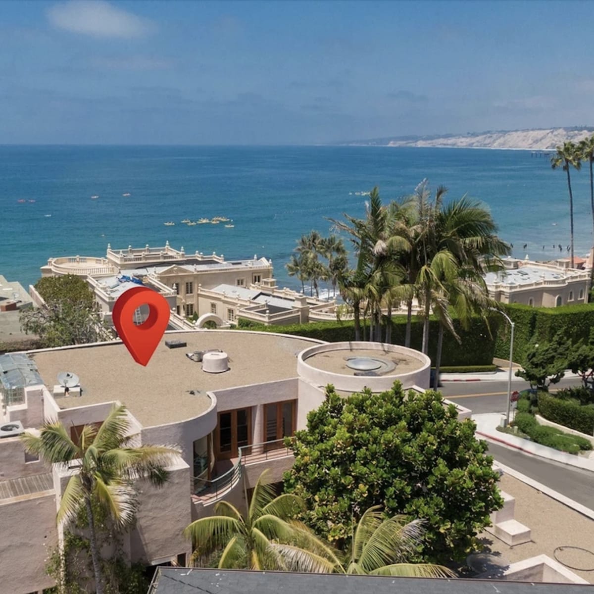 A coastal view with a red location pin indicating a property near the ocean, surrounded by palm trees and other buildings.