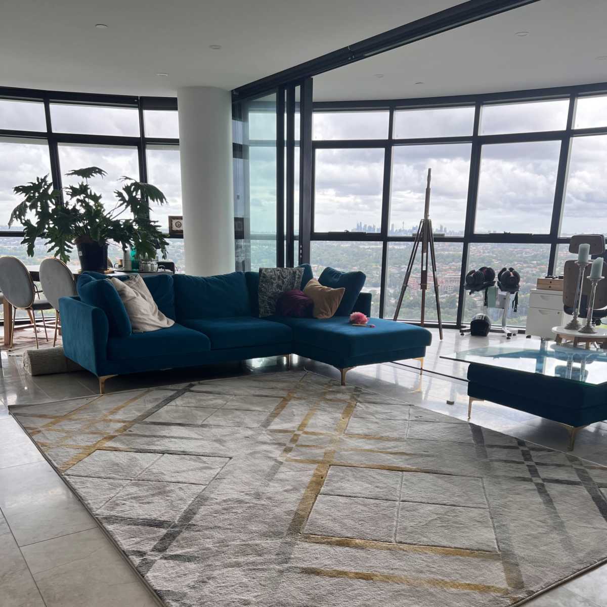 A contemporary living room with a large turquoise sectional sofa, a geometric area rug, and large windows offering a city view.