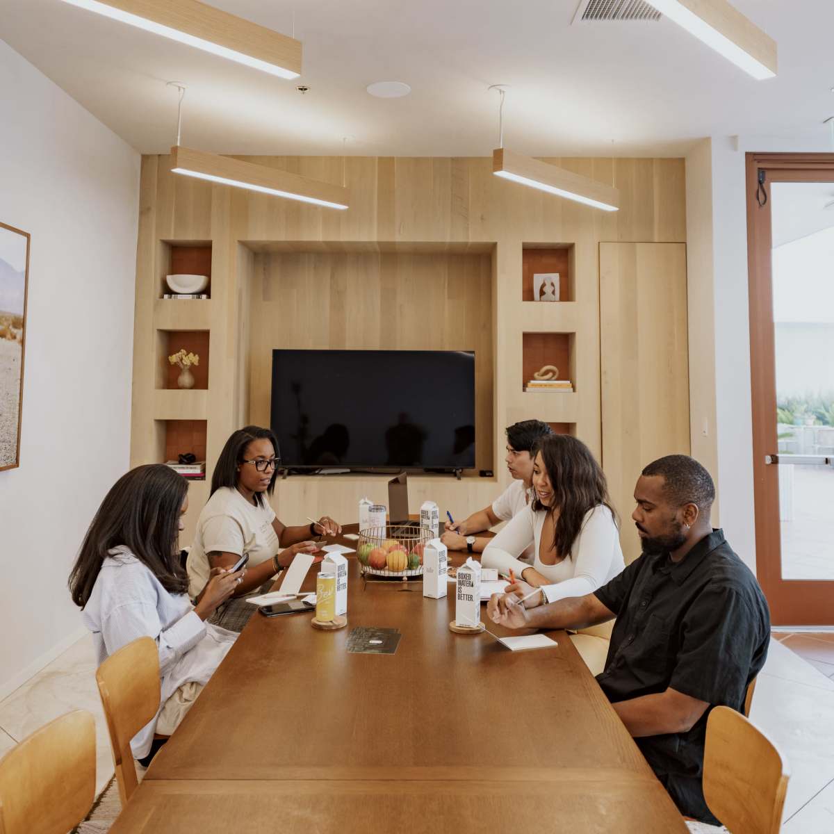 A group of five people is seated around a wooden table in a conference room, engaged in a discussion while various beverages are placed on the table.