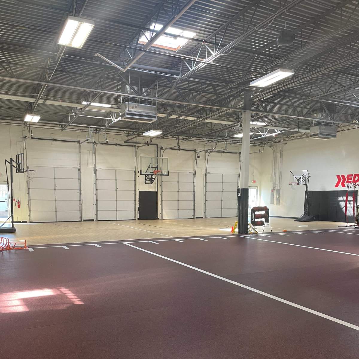 An indoor basketball court with a reddish floor, several basketball hoops, and a spacious, well-lit area.
