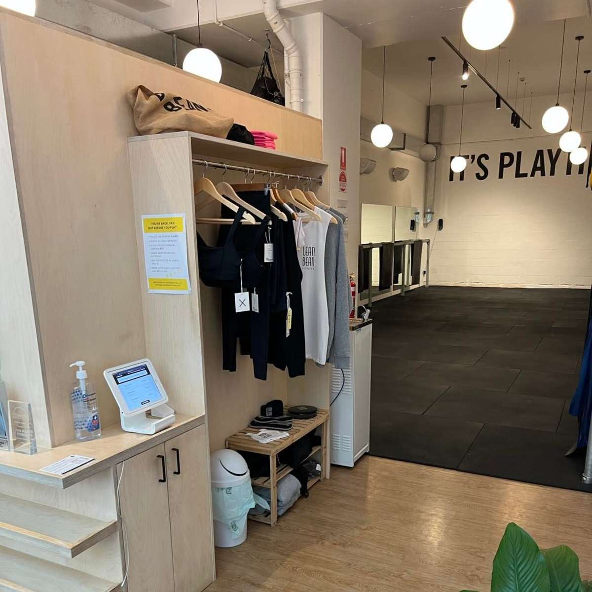 The interior of a fitness studio with a neatly arranged reception area featuring clothing racks and a hand sanitizer station.