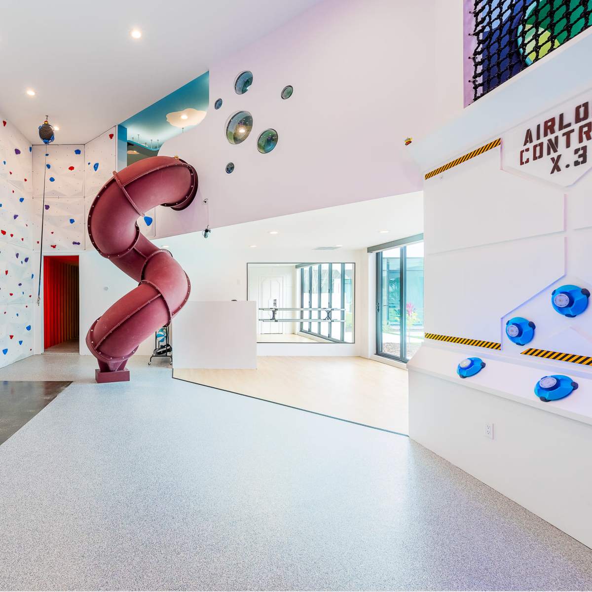 A modern recreational space featuring a climbing wall, a basketball hoop, and a spiral slide.