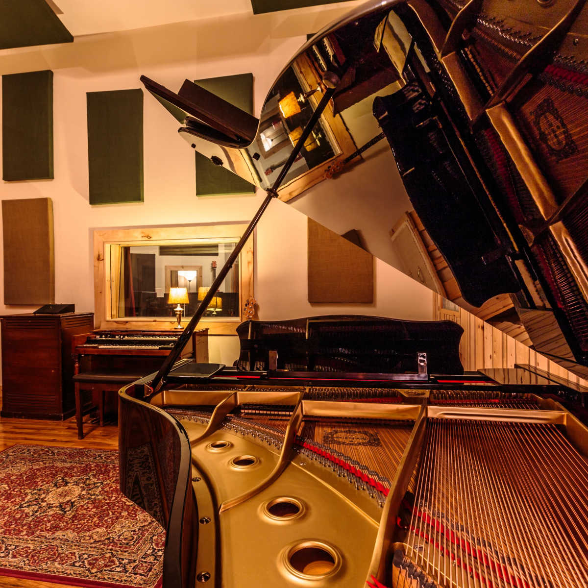A music recording studio featuring a grand piano, a vintage console, and acoustic panels on the walls.