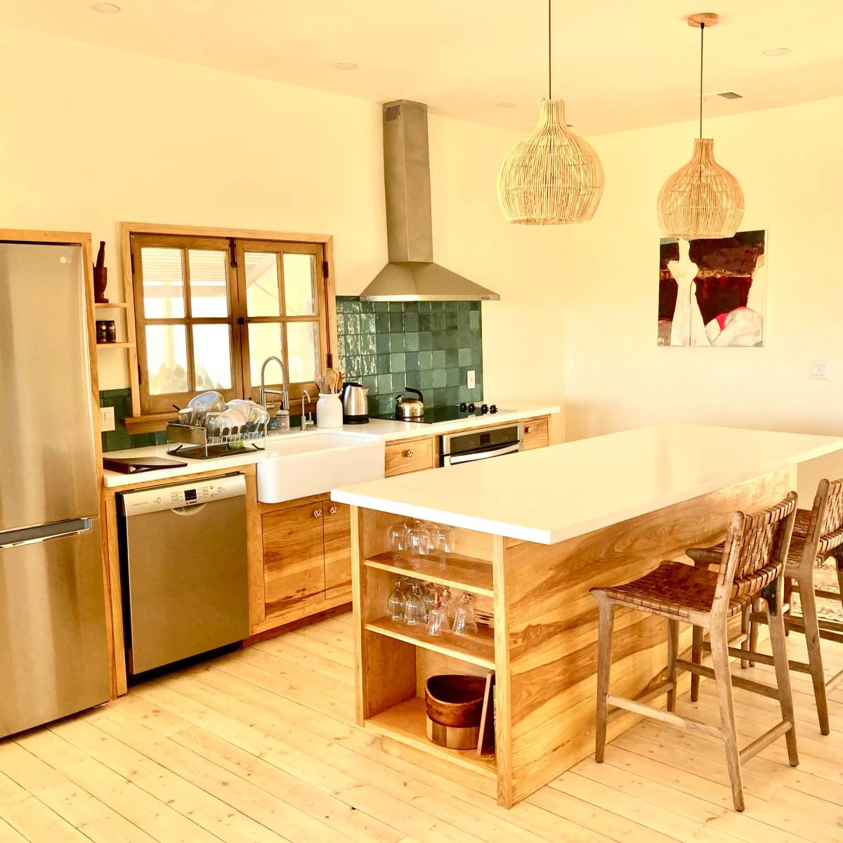 A modern kitchen features a large island with bar stools, stainless steel appliances, wooden cabinetry, and pendant lighting.