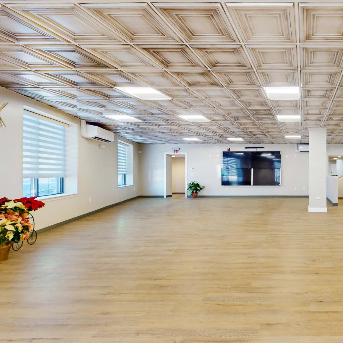 A spacious interior room with wooden flooring, decorative ceiling panels, and minimal furnishings.