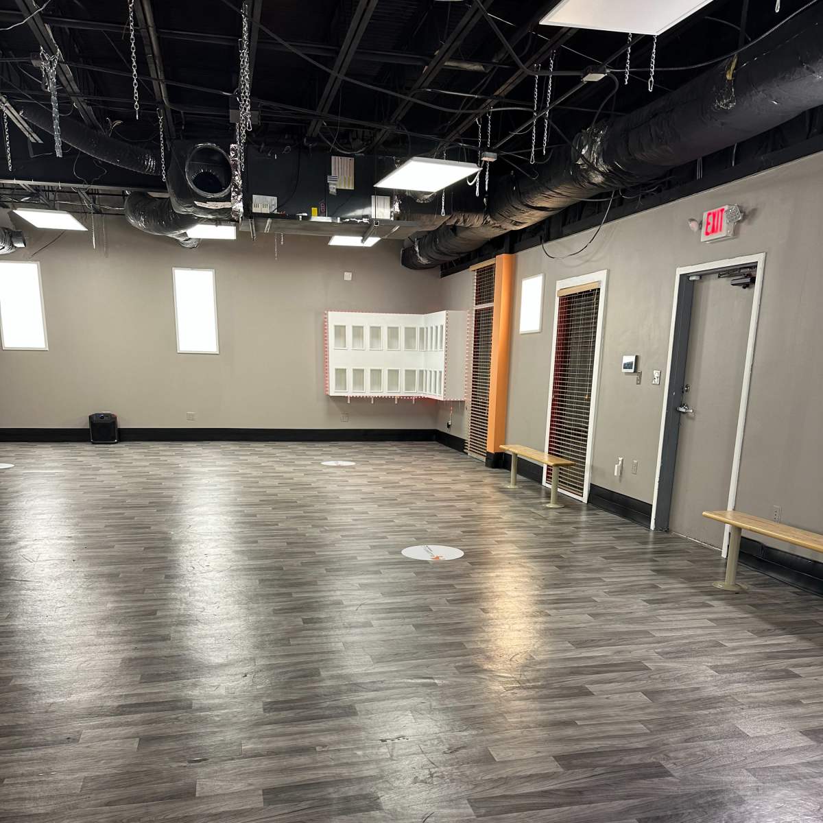 An empty indoor space with a wooden floor, bright lighting, and several benches along the walls.