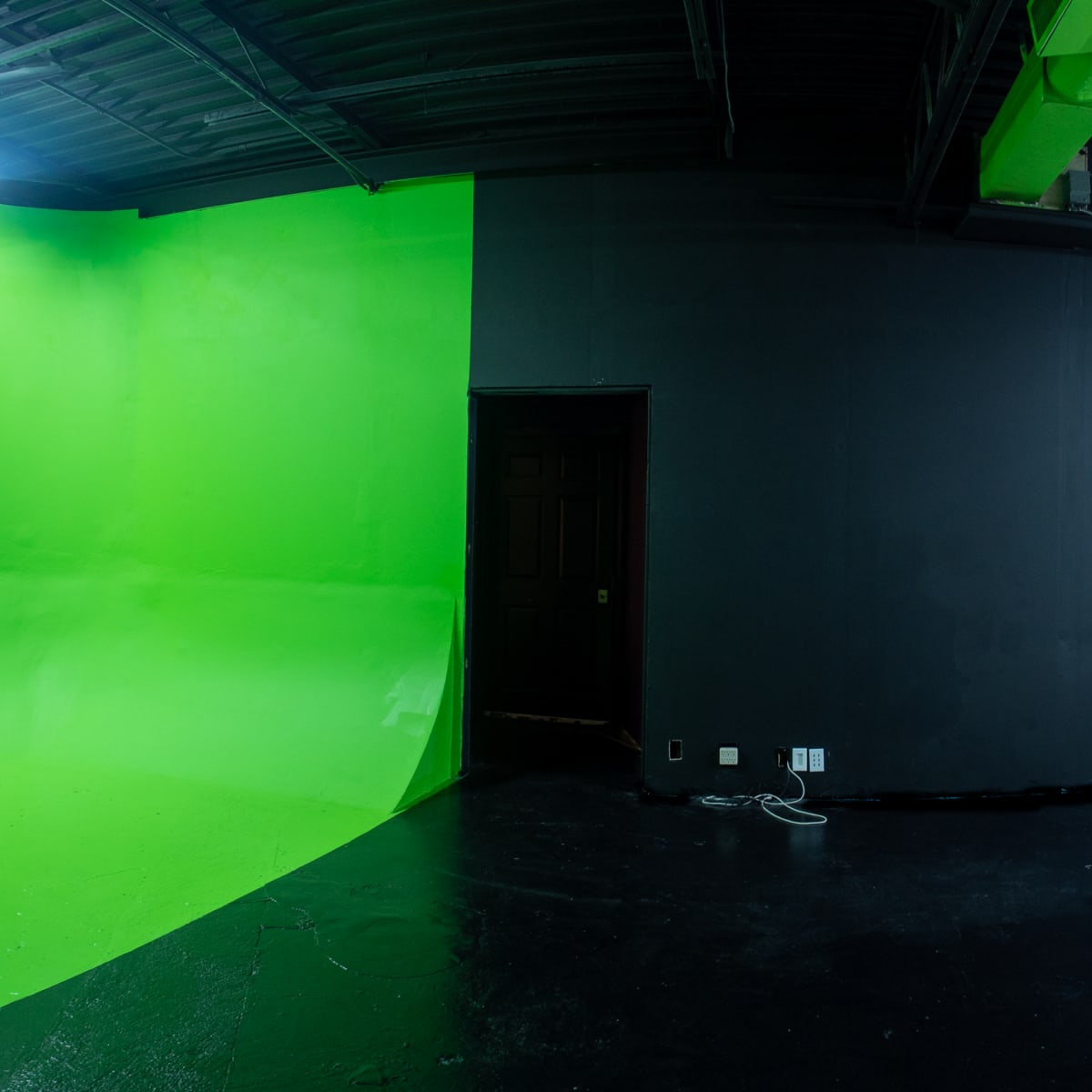 A studio space with a green screen on one wall, a black painted wall opposite, and a white floor.