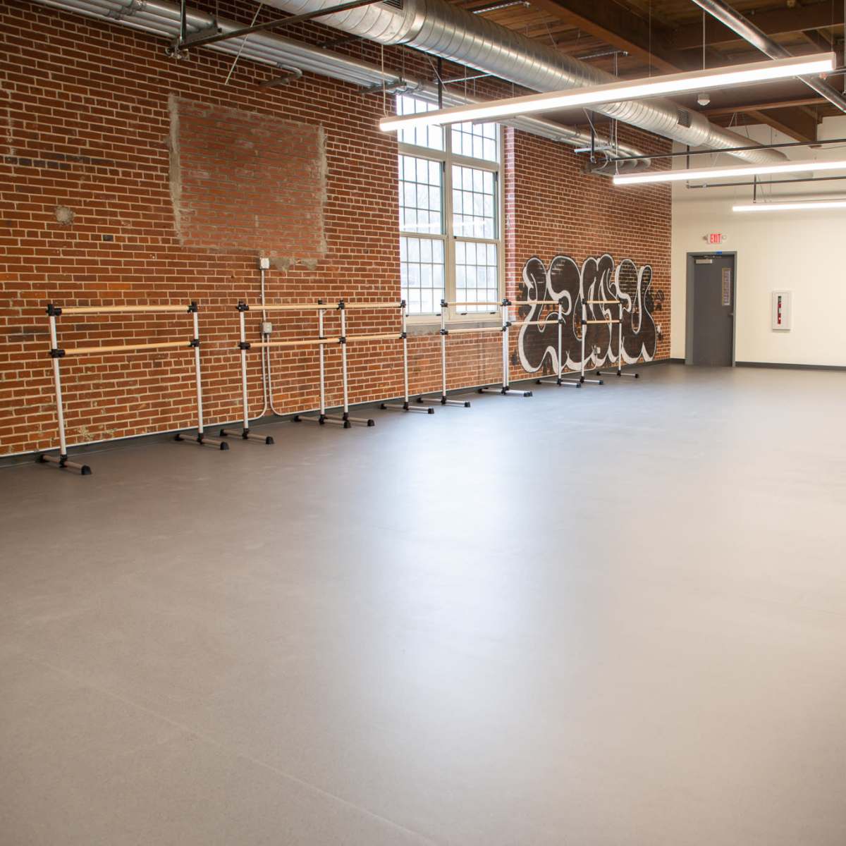 A spacious dance studio with wooden beams, exposed brick walls, and several ballet barres along one side.