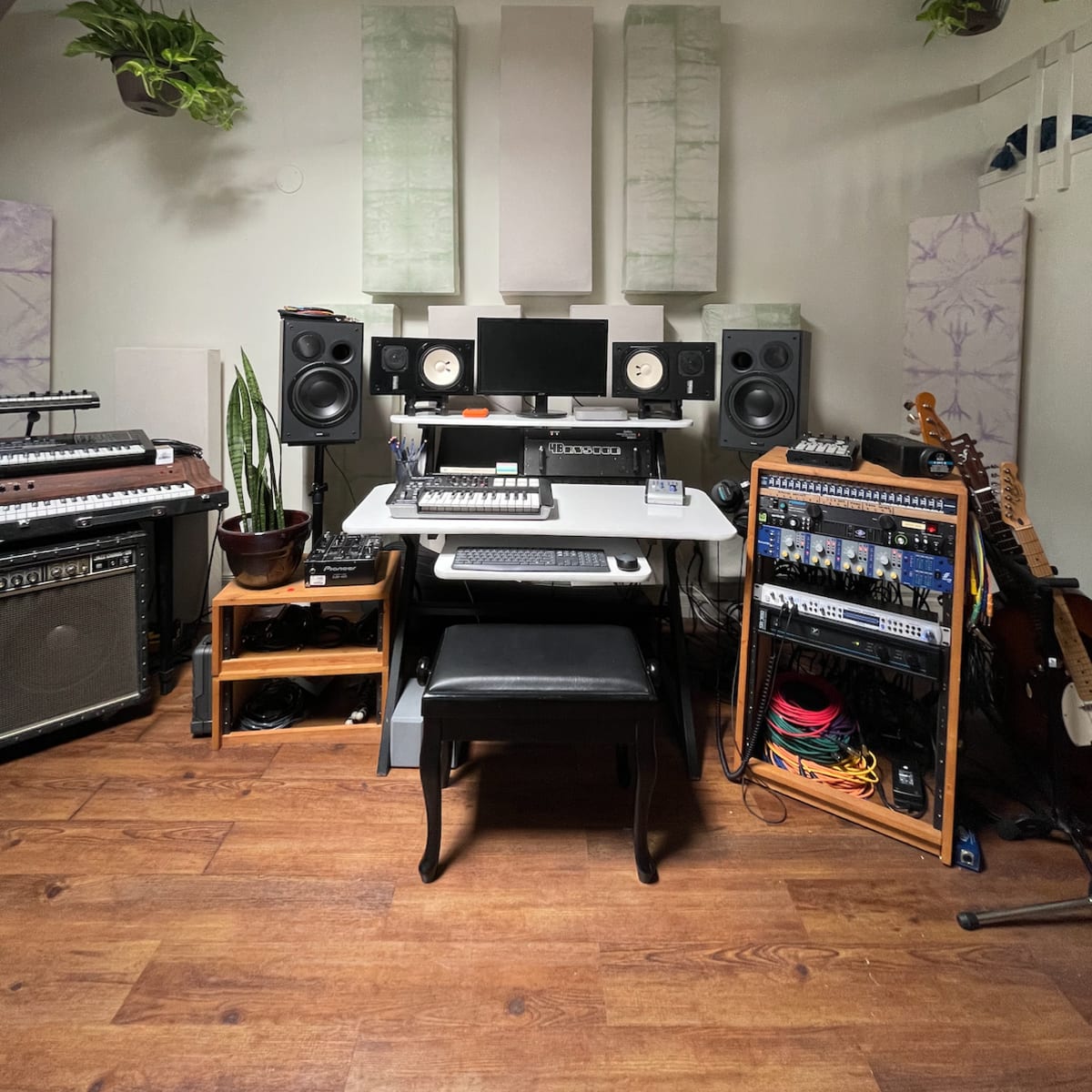 A music production studio with a desk setup, speakers, and various musical equipment arranged on the walls and shelves.