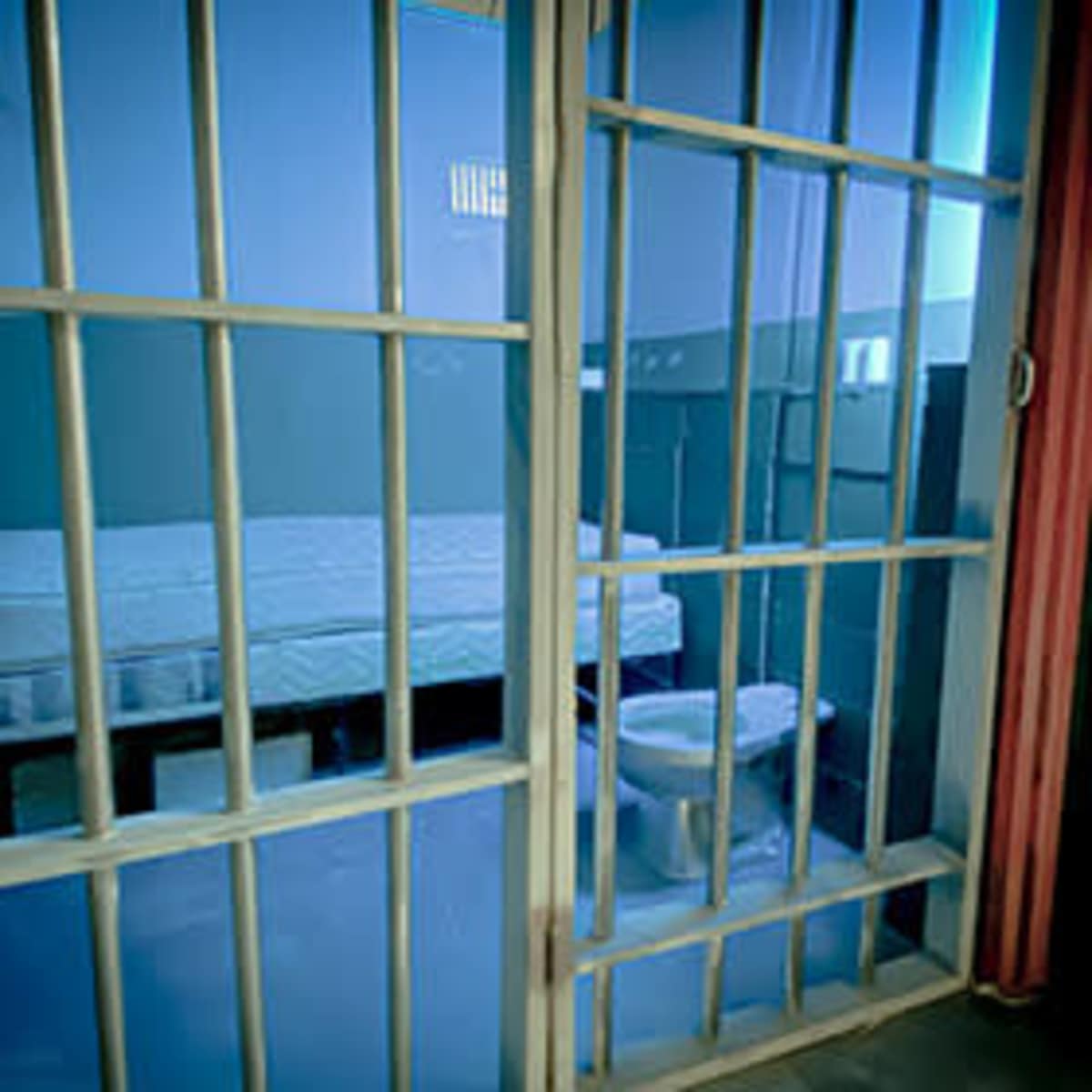 The interior of a prison cell with barred doors, a bed, and a toilet.