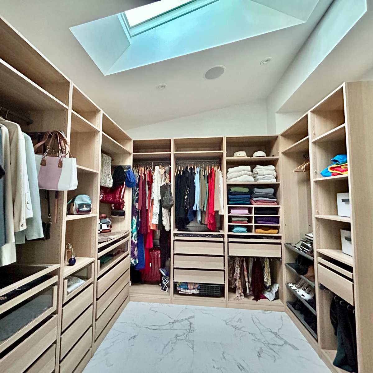 A spacious walk-in closet features organized shelves and hanging areas filled with clothing and accessories, illuminated by a skylight above.