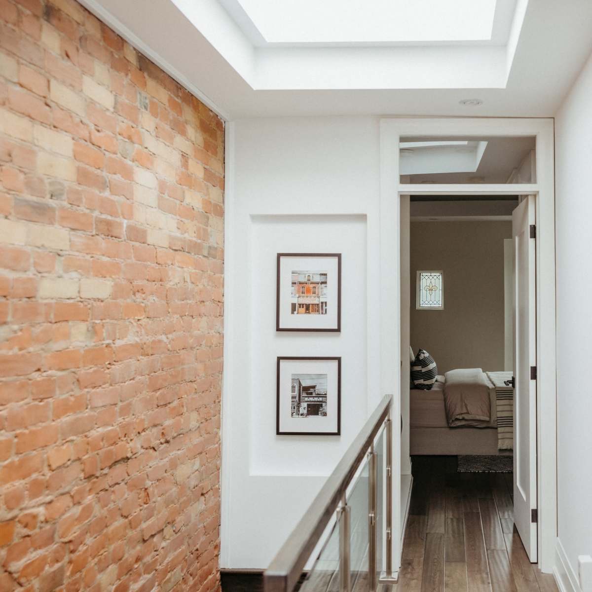 A hallway with exposed brick walls, framed pictures, and doors leading to a bedroom and a bathroom.
