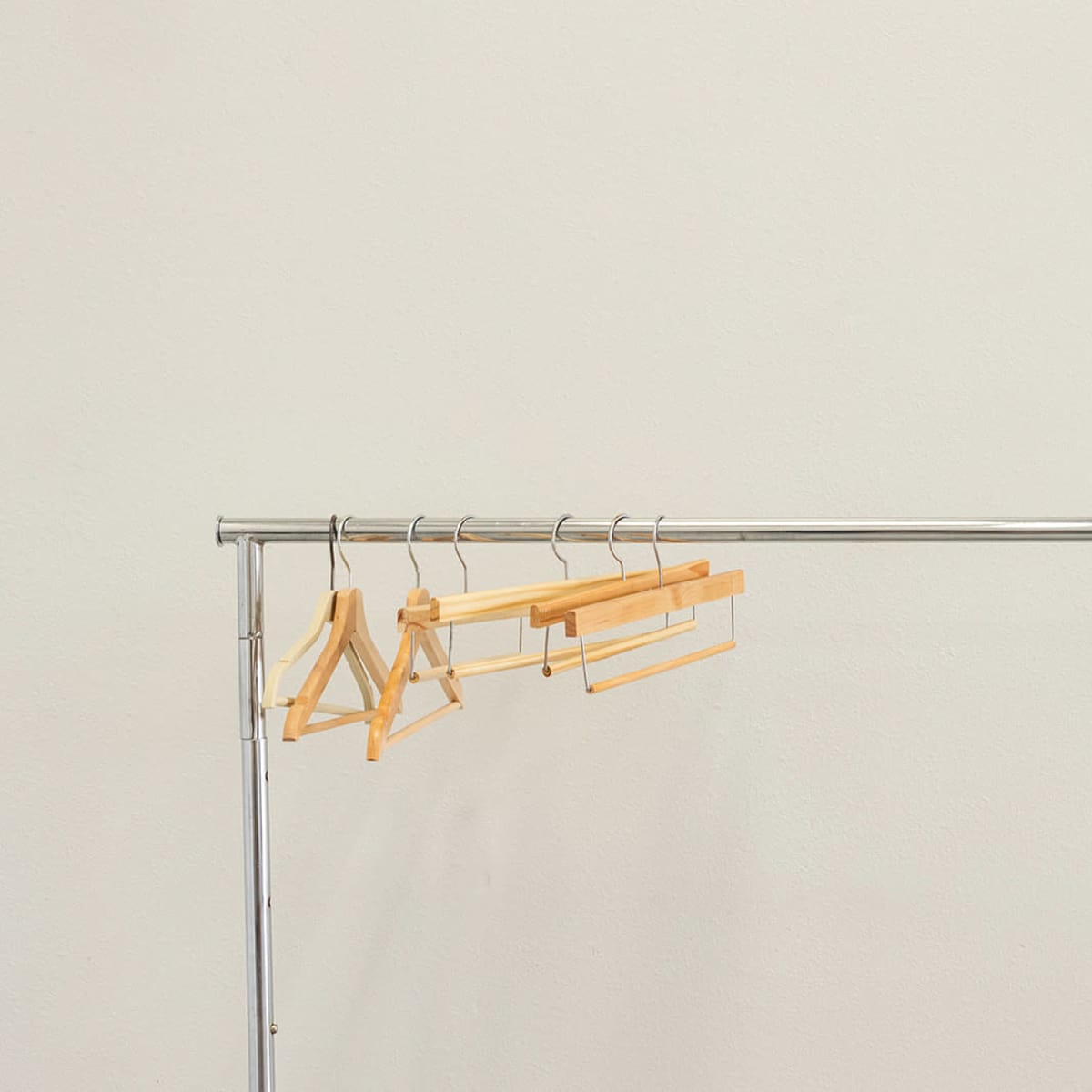 A chrome clothing rack displays several wooden hangers against a plain white wall.