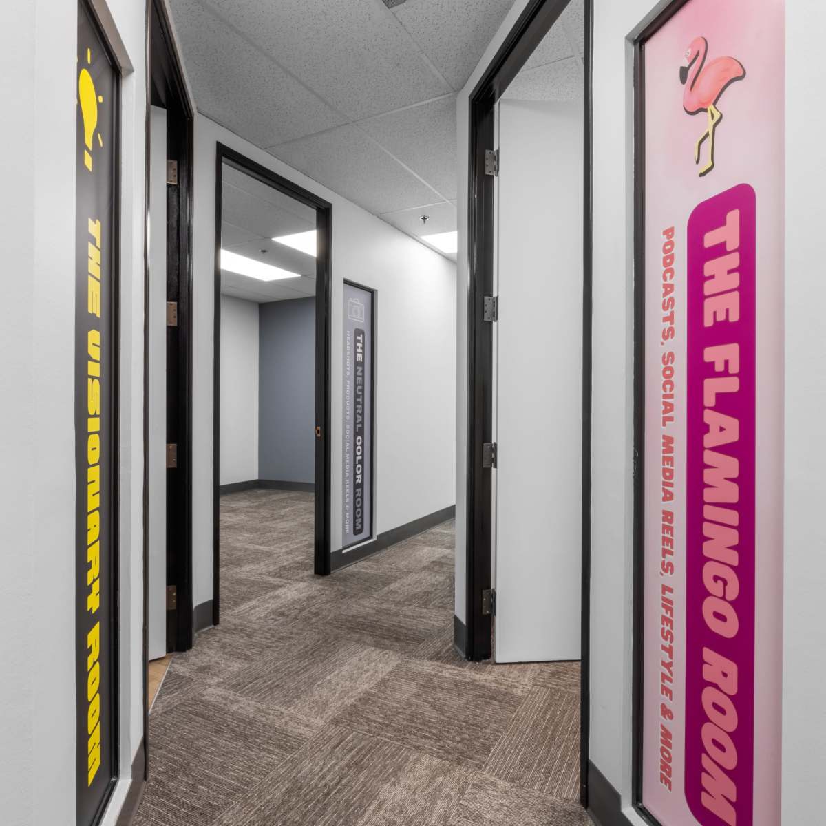 A hallway with two open doors featuring colorful signs labeled "The Visionary Room" and "The Flamingo Room."