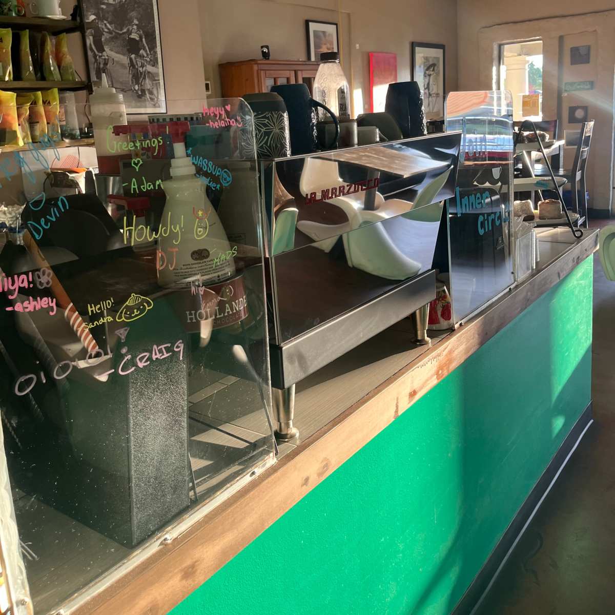 A restaurant interior with tables and chairs, and a counter displaying handwritten messages on the glass partition.