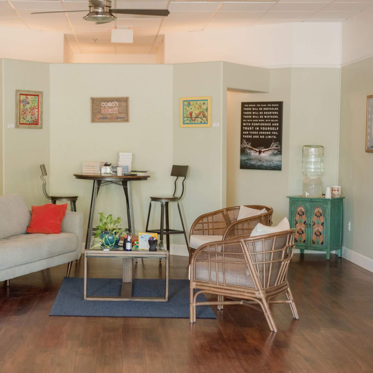 A modern waiting area with a grey sofa, two rattan chairs, a glass coffee table, and decorative wall art.