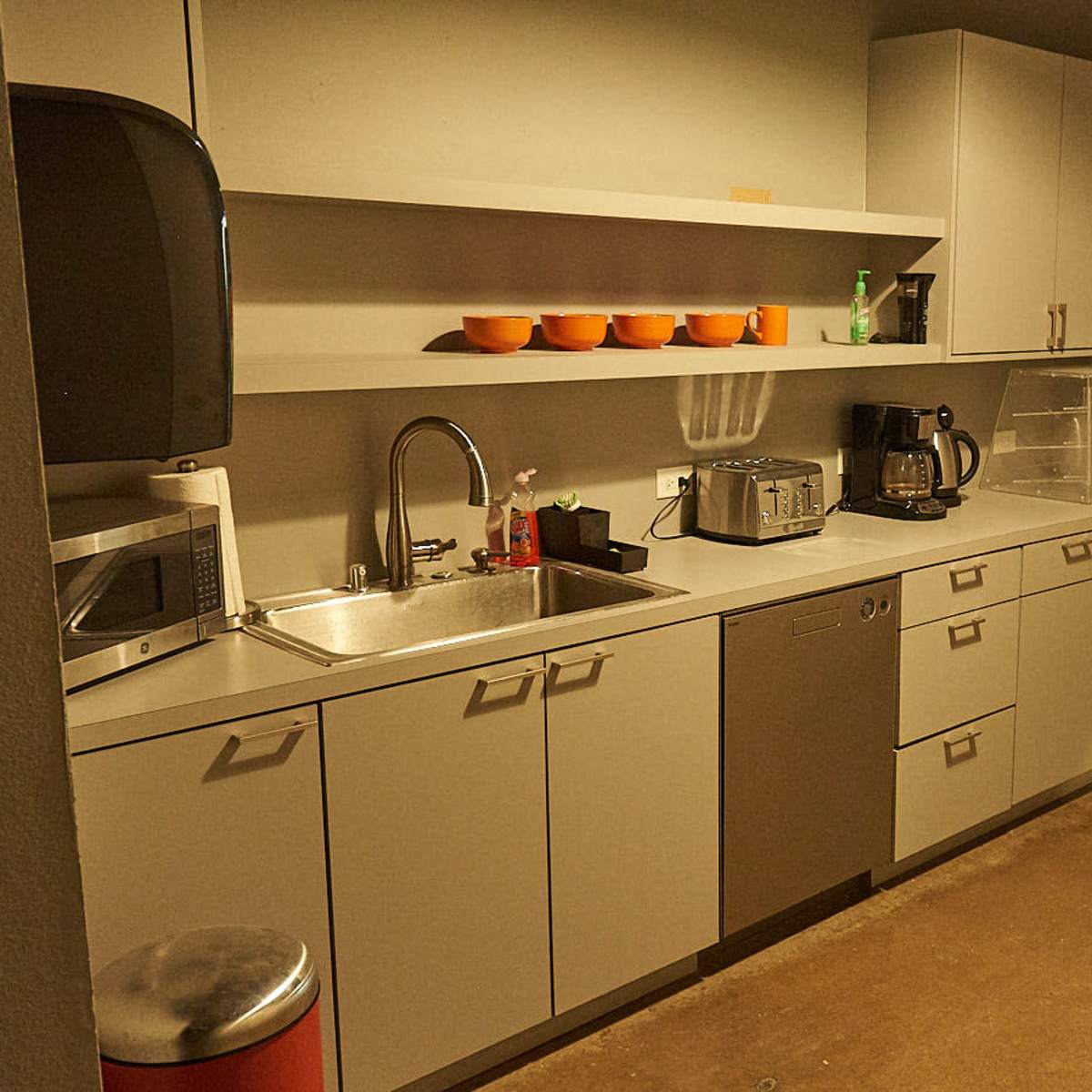 A modern kitchen with gray cabinets, stainless steel appliances, and a counter featuring a sink, microwave, and coffee maker.
