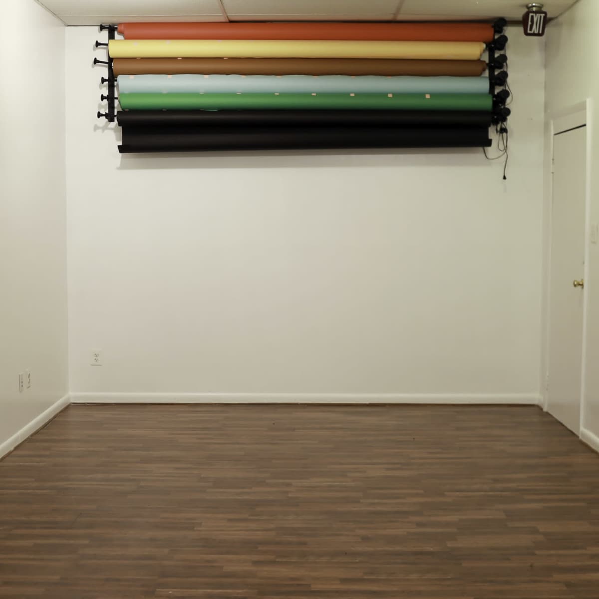 A minimalistic studio space featuring a wooden floor and a wall-mounted backdrop with horizontal colored rolls above it.