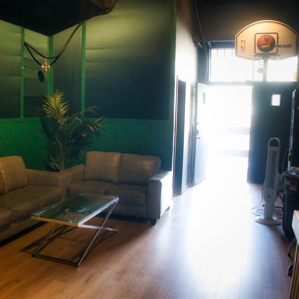A green-walled room with a brown couch, a glass coffee table, and a doorway leading outside.