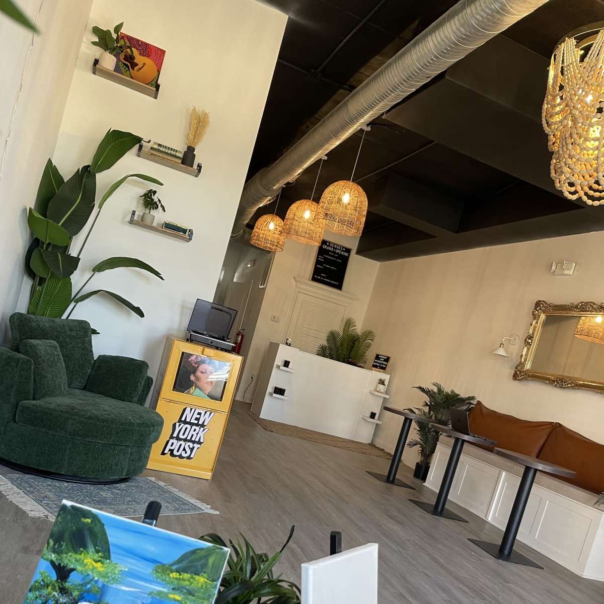 A modern interior space with a green upholstered chair, two blank easels, a decorative plant, and pendant lighting.