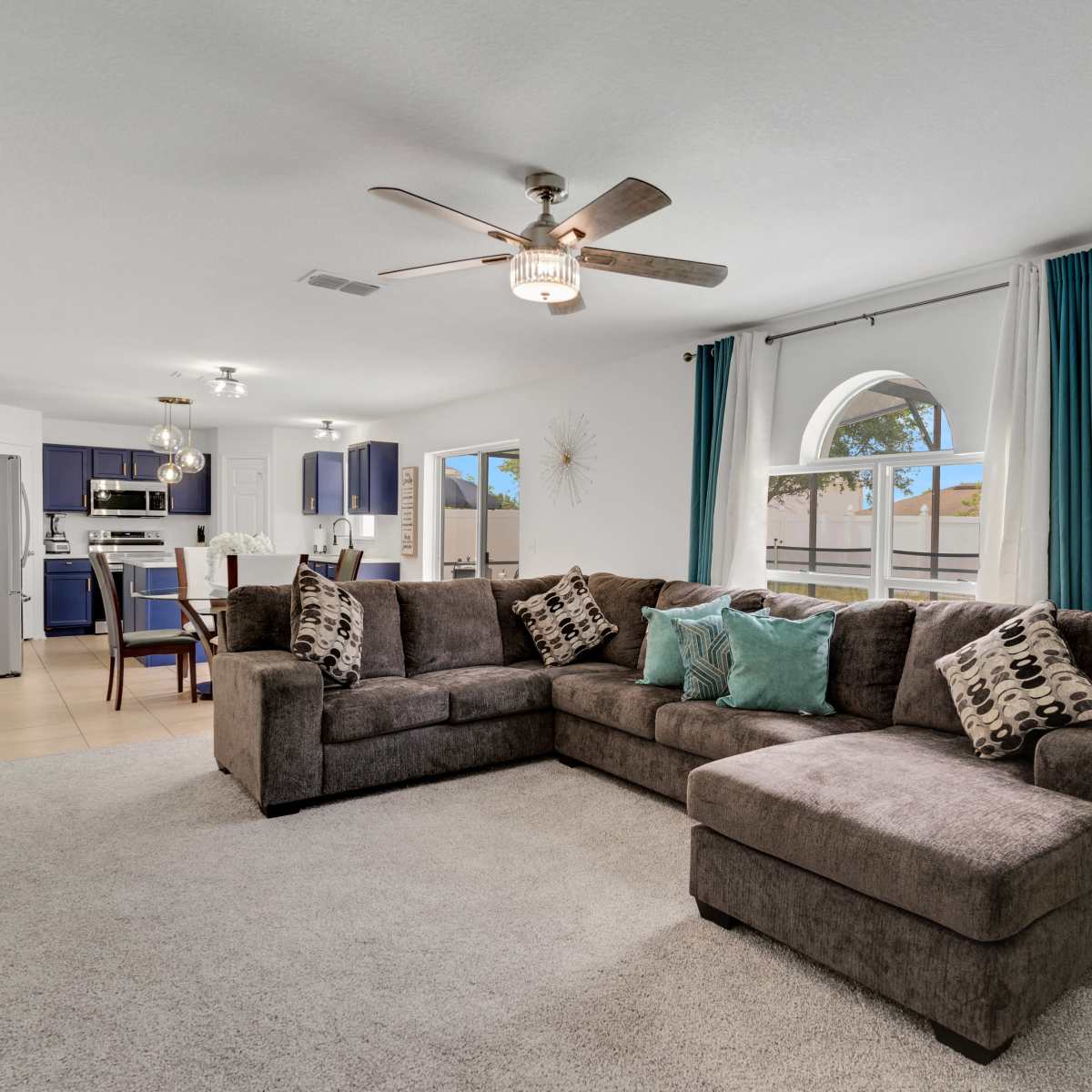 A living room with a large sectional sofa, a coffee table, and a kitchen area visible in the background.