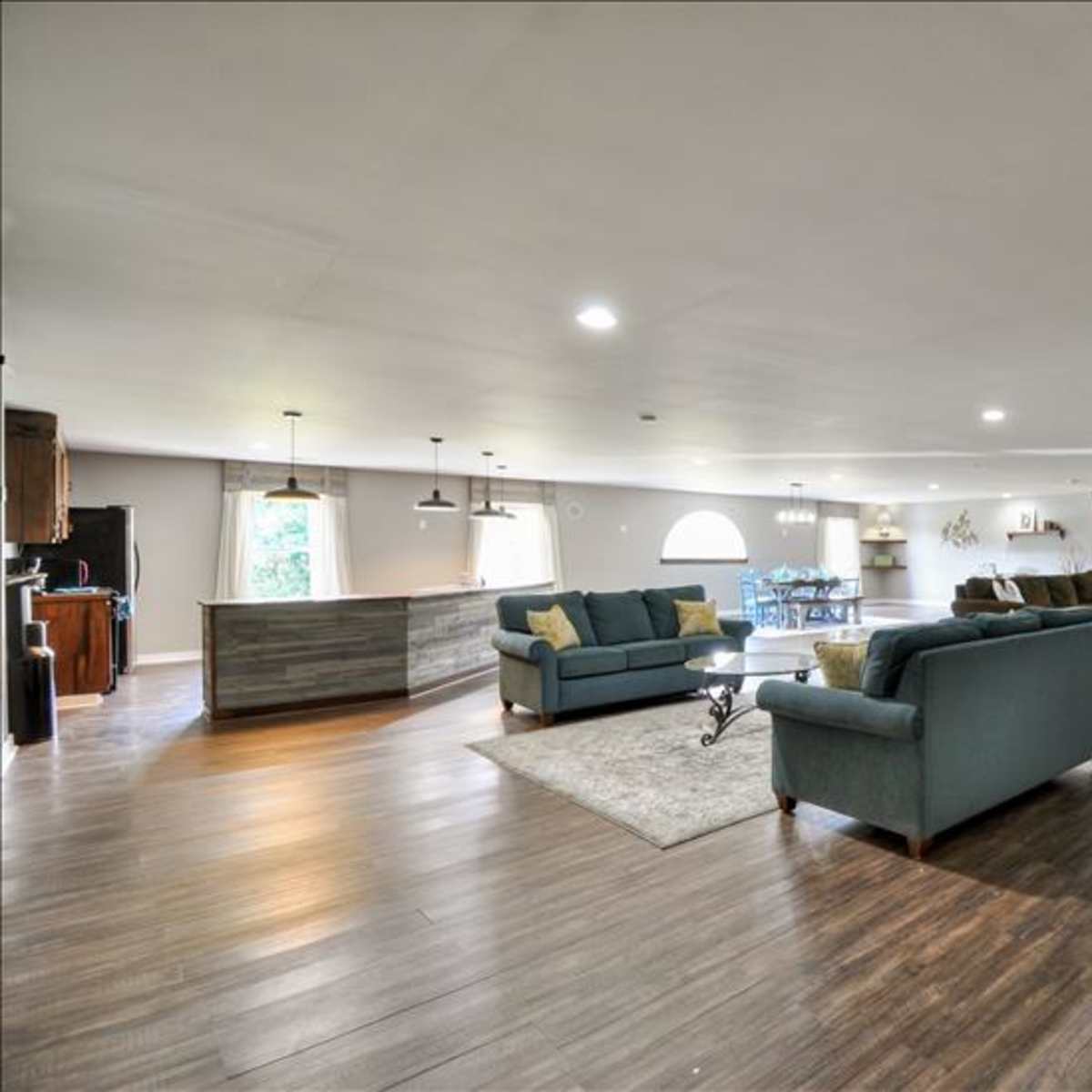 A spacious living area with two sets of sofas, a small dining table, and a kitchen bar in an open layout.