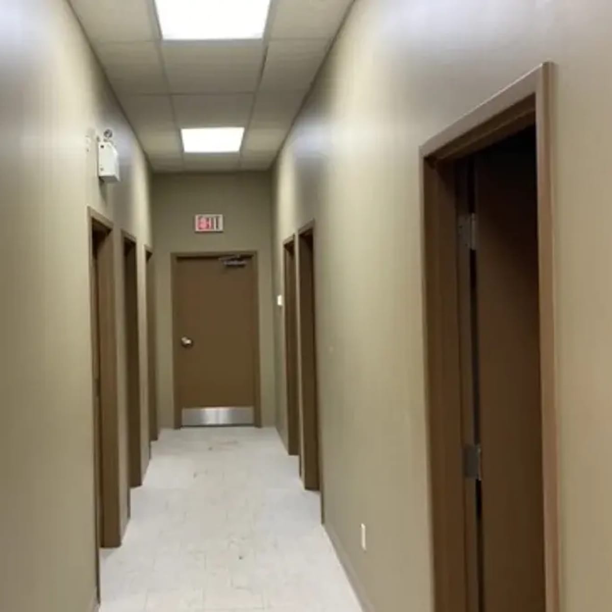 A narrow hallway with several doorways on either side and an exit door at the end.