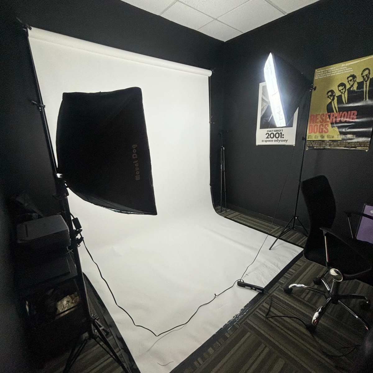 A photography studio with a white backdrop, studio lights, and a black office chair in a dimly lit room.