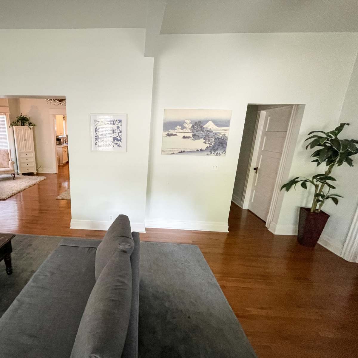 A light-filled living room with a gray sofa, a wooden coffee table, and an open doorway leading to another room.