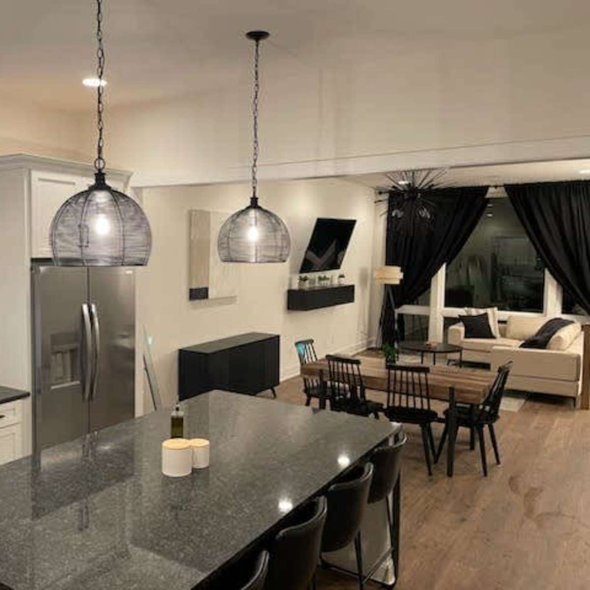 A modern kitchen and dining area with a large island, stainless steel appliances, and a connected living room featuring a sofa and a television.