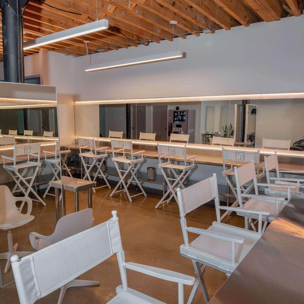 A spacious room with several white director's chairs arranged in front of a long mirror under bright lighting.