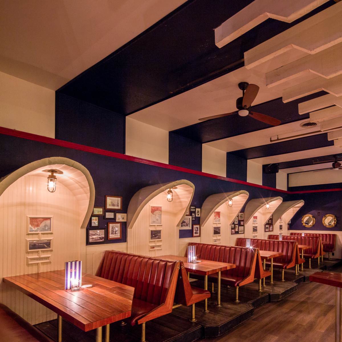 The interior of a restaurant features wooden booths with arched backs, framed pictures on the walls, and ceiling fans.