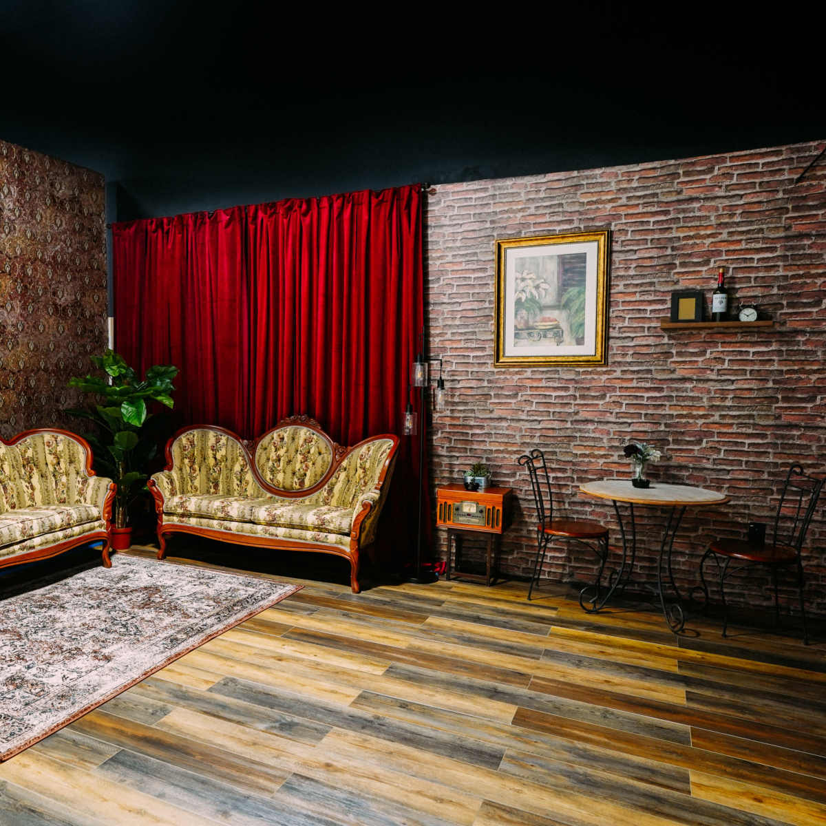 A vintage-style sitting area with floral-patterned sofas, a circular table, and a backdrop of brick and patterned wallpaper.