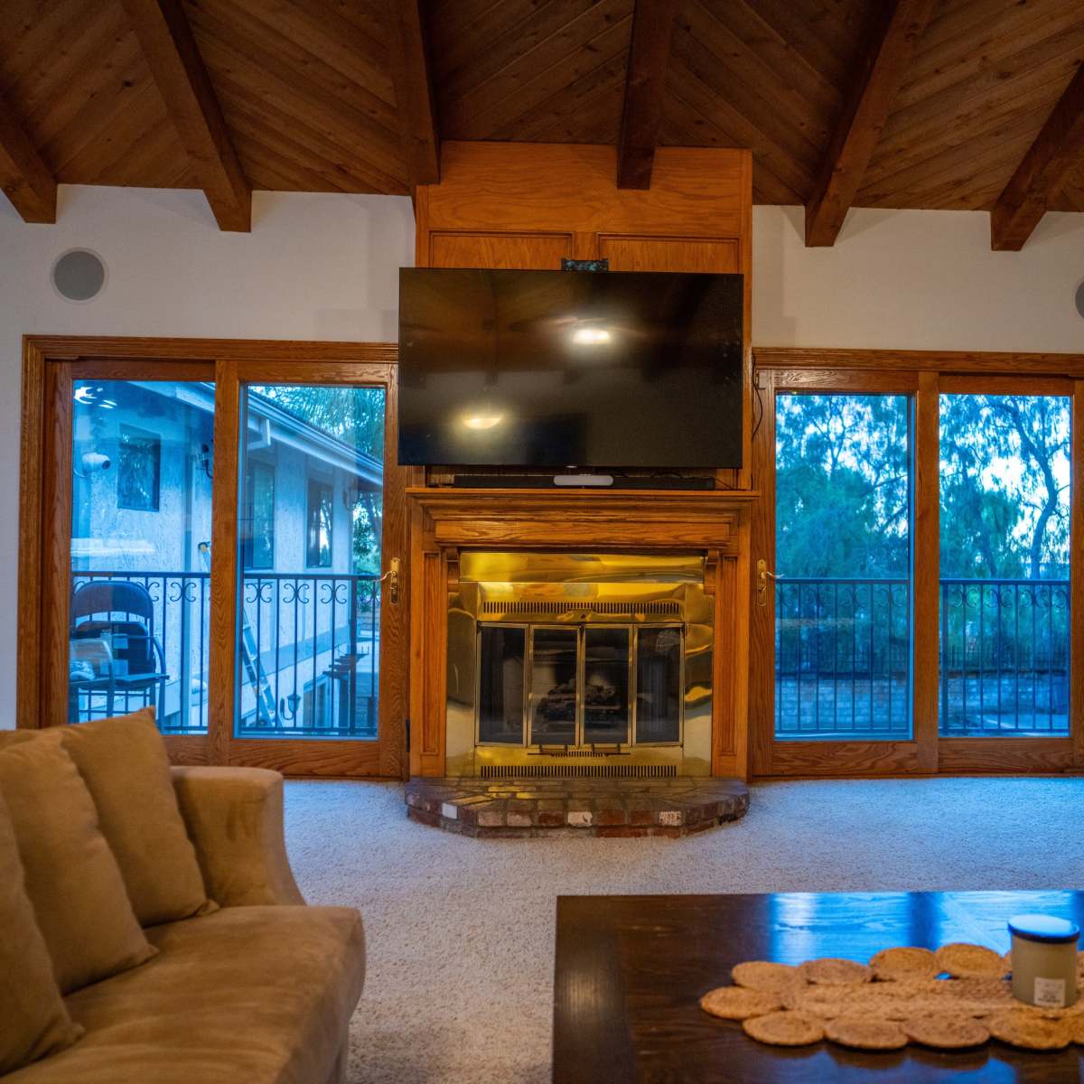 The living room features a stone fireplace with a mounted television above it, flanked by large windows that provide views of the outdoors.