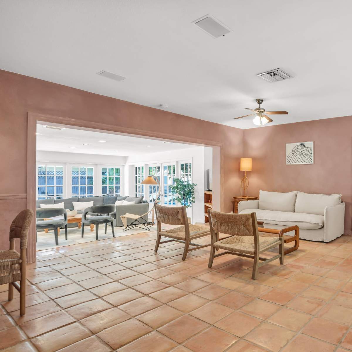 The room features a seating area with a sofa, chairs, and a ceiling fan, surrounded by tiled flooring and a doorway leading to another space.