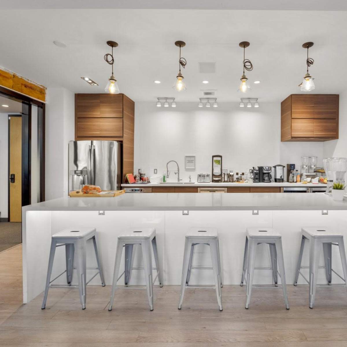 A modern kitchen features a large central island with six metal stools, surrounded by wooden cabinets and various kitchen appliances.