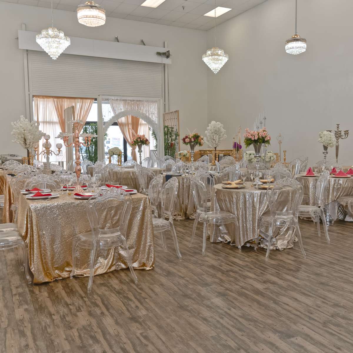A banquet hall set up with multiple tables covered in gold tablecloths and adorned with floral centerpieces.
