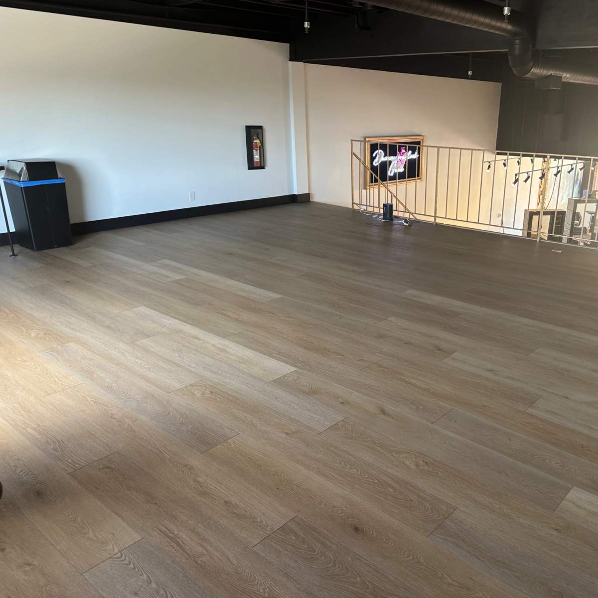 An empty, well-lit room with wooden flooring and large windows along one wall.