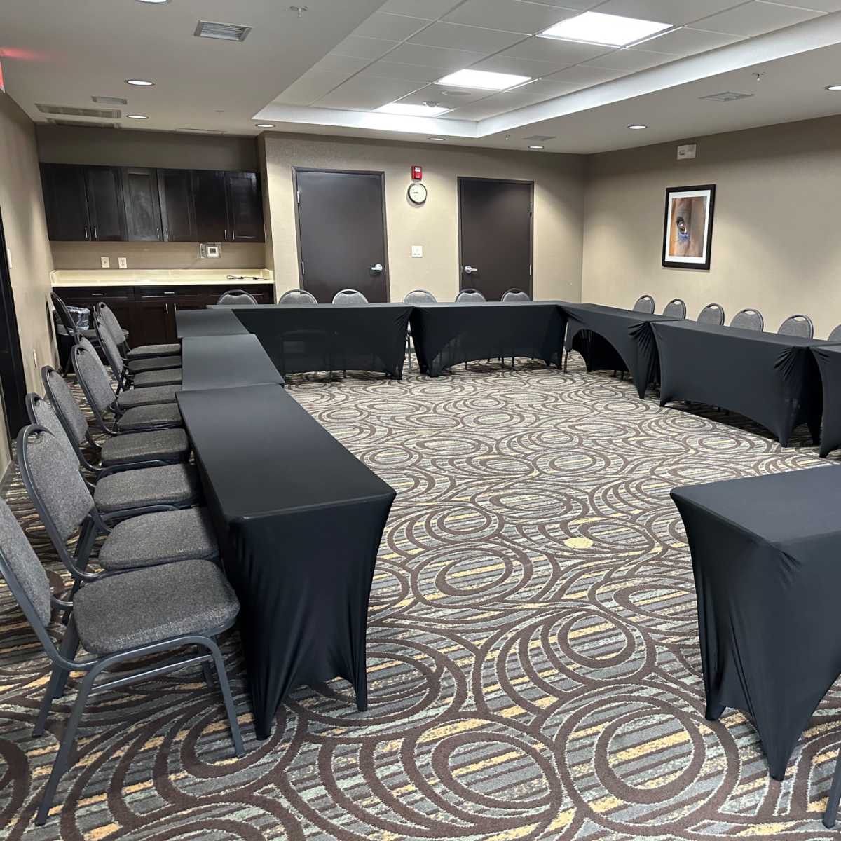 A conference room set up with a large U-shaped arrangement of tables covered in black cloth, surrounded by gray chairs.