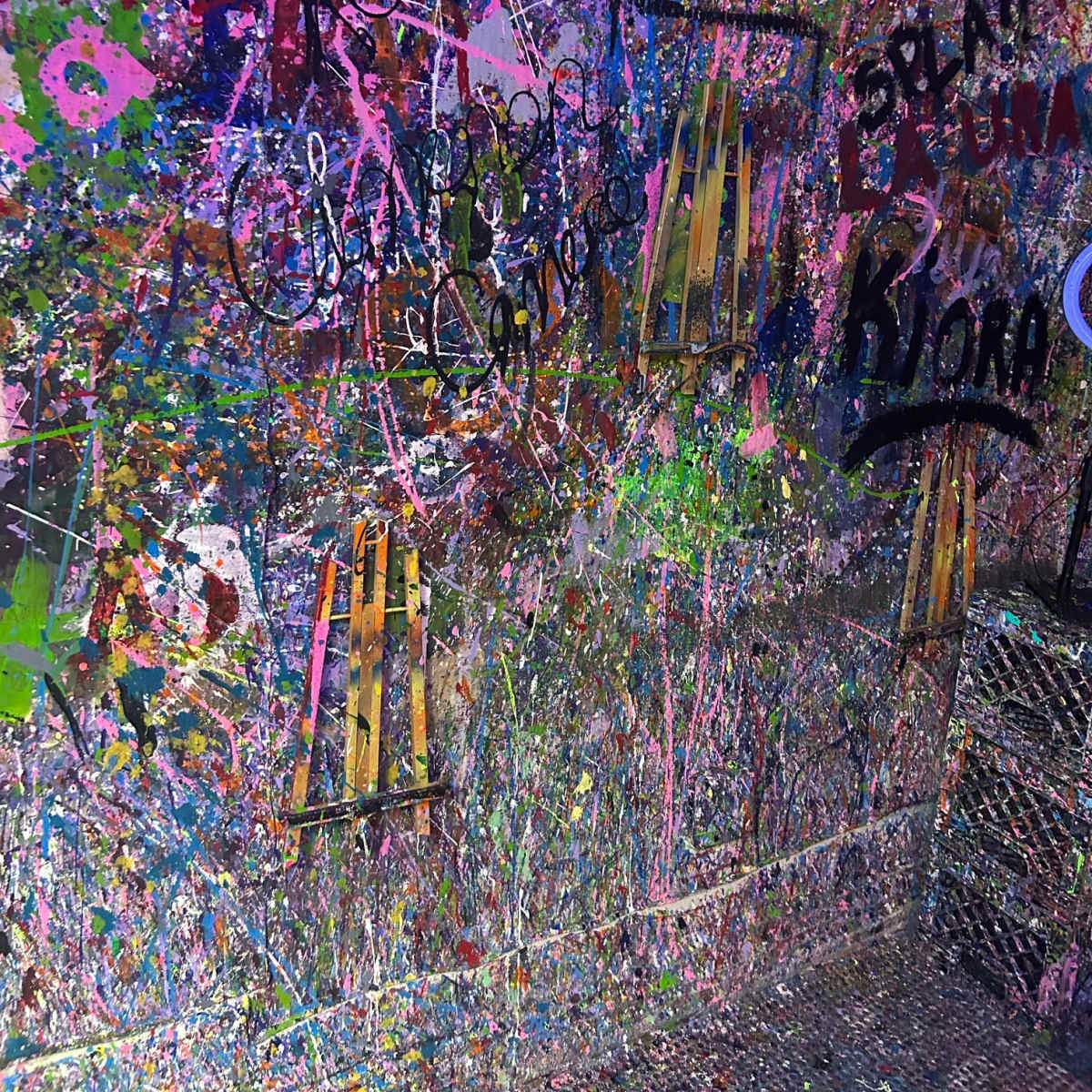 The wall is covered in a chaotic array of colorful paint splatters and graffiti tags.